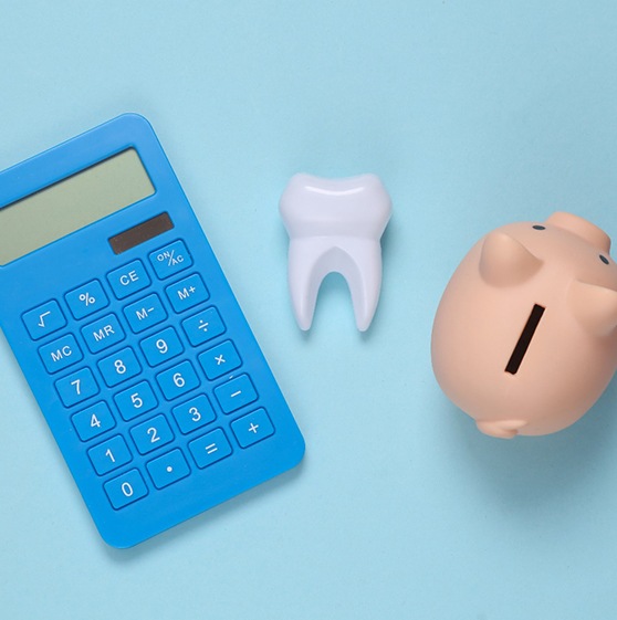 Calculator on desk next to piggy bank and model of tooth