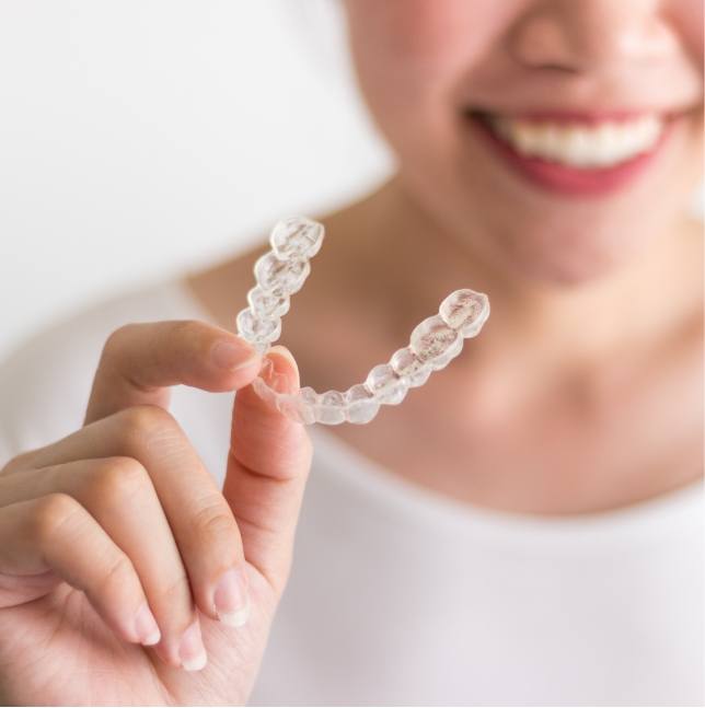 Smiling woman holding an Invisalign aligner