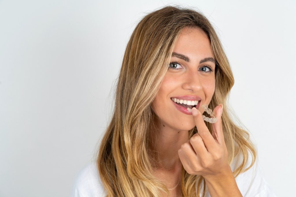 Woman smiling while holding Invisalign aligner